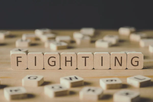 Selective focus of fighting inscription on cubes surrounded by blocks with letters on wooden surface isolated on black — Stock Photo