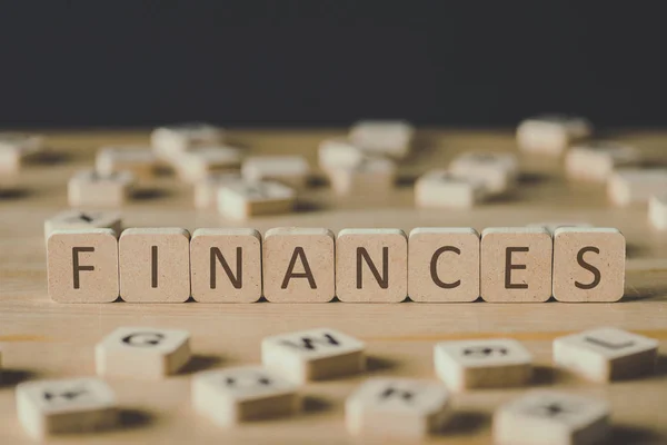 Selective focus of finances inscription on cubes surrounded by blocks with letters on wooden surface isolated on black — Stock Photo