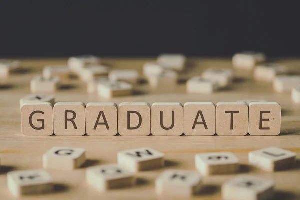 Selective focus of graduate lettering on cubes surrounded by blocks with letters on wooden surface isolated on black — Stock Photo