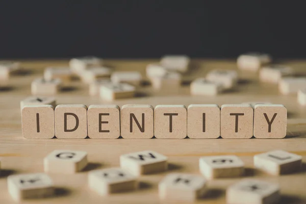 Enfoque selectivo de la palabra identidad hecha de cubos rodeados de bloques con letras en la superficie de madera aislada en negro - foto de stock