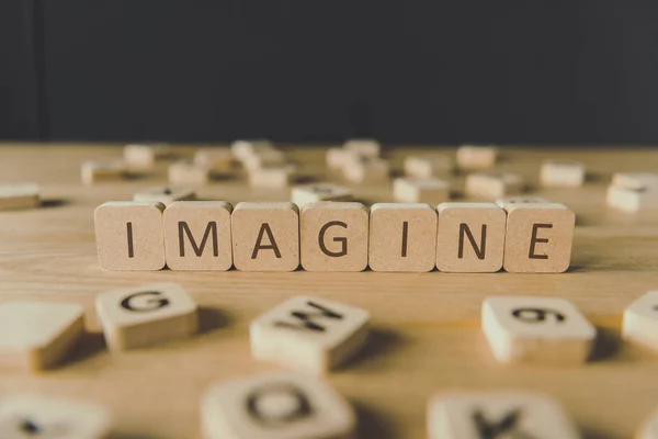 Enfoque selectivo de la palabra imaginar hecho de cubos rodeados de bloques con letras en la superficie de madera aislada en negro - foto de stock