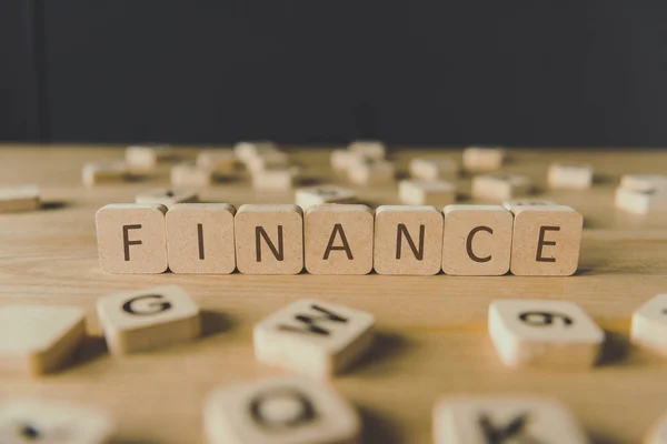 Selektive Fokussierung der Finanzinschrift auf Würfel, umgeben von Blöcken mit Buchstaben auf hölzerner Oberfläche, isoliert auf schwarz — Stockfoto