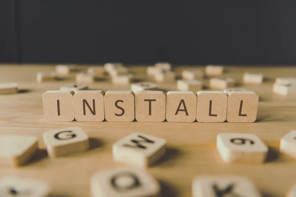 Selective focus of cubes with word install surrounded by blocks with letters on wooden surface isolated on black — Stock Photo