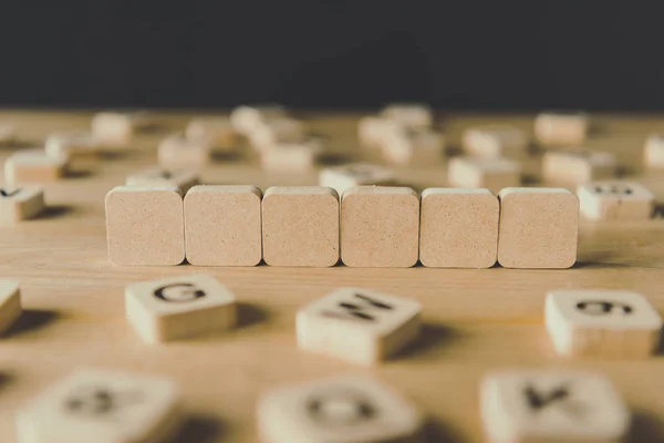 Foyer sélectif de six cubes vides entourés de blocs avec des lettres sur la surface en bois isolé sur noir — Photo de stock