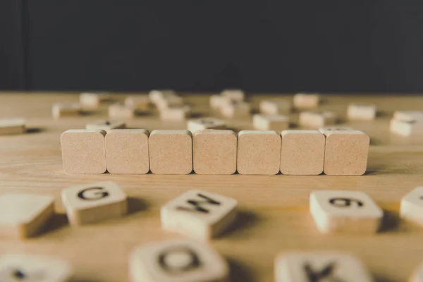 Selective focus of seven blank cubes surrounded by blocks with letters on wooden surface isolated on black — Stock Photo