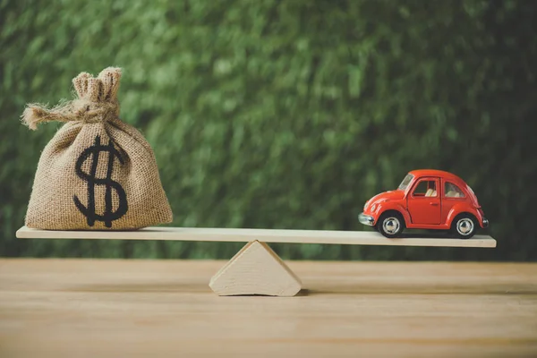 Toy car and money bag with dollar sign balancing on seesaw on green background — Stock Photo