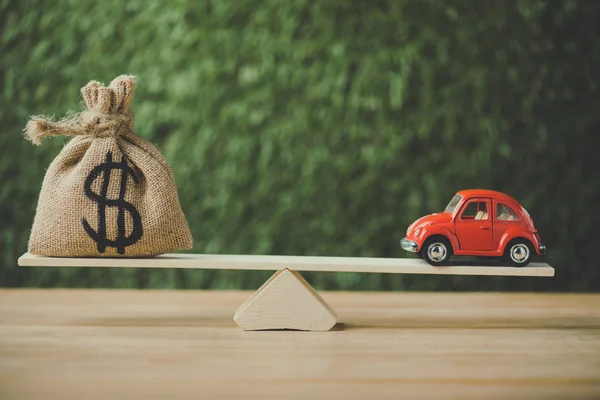 Juguete coche y bolsa de dinero con signo de dólar balanceo en balancín sobre fondo verde - foto de stock