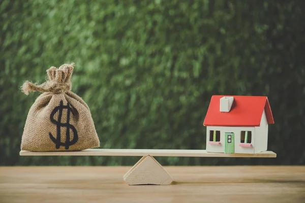 Money bag with dollar symbol and house model balancing on swing on green background — Stock Photo