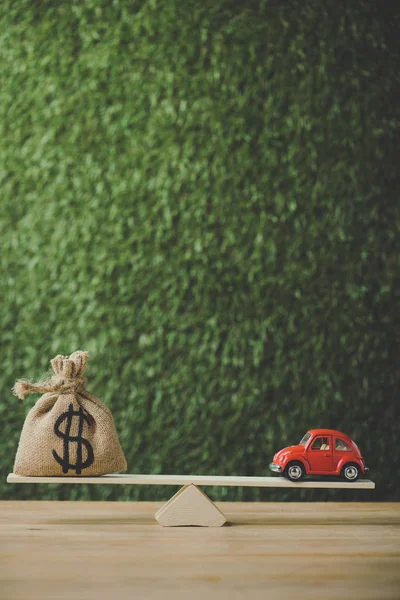 House model and money bag with dollar symbol balancing on seesaw on green background — Stock Photo