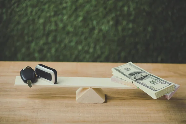 Pack of dollar banknotes and car key balancing on swing on green background — Stock Photo