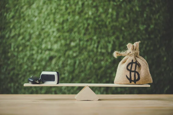 Money bag with dollar sign and car key balancing on seesaw on green background — Stock Photo