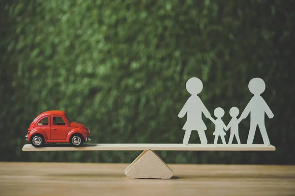 Red miniature car and paper cut family balancing on swing on green background — Stock Photo