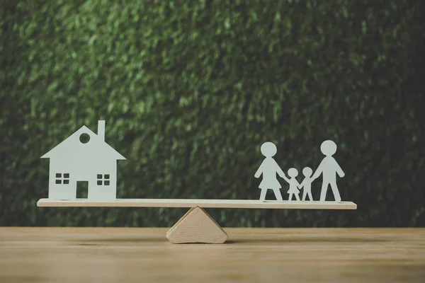 Casa de corte de papel y familia de papel equilibrio en balancín sobre fondo verde - foto de stock