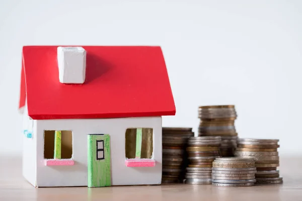 House model with red roof and white walls and stacks of metal coins isolated on grey — Stock Photo