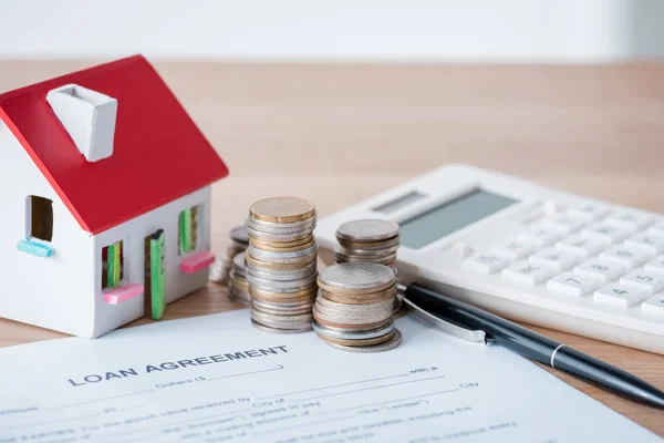 Modelo de casa, monedas de plata y oro, contrato de préstamo y calculadora en superficie de madera - foto de stock