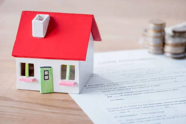 Modelo de casa, contrato de préstamo y pilas de monedas de metal en la superficie de madera - foto de stock