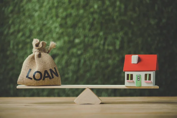 Money bag with dollar symbol and house model balancing on swing on green background — Stock Photo