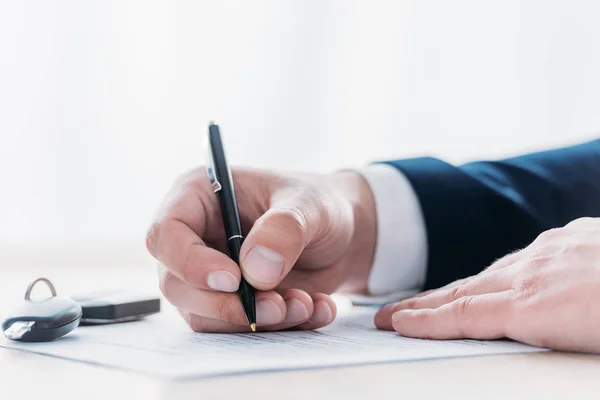 Vue partielle de l'homme d'affaires tenant stylo et écriture dans l'accord de prêt et clés de voiture sur la table — Photo de stock