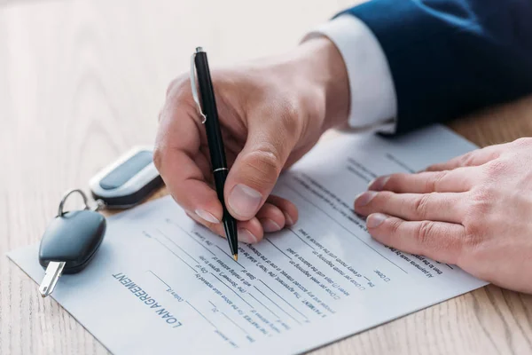 Vista parcial del gerente escribiendo en el contrato de préstamo y las llaves del coche en la mesa — Stock Photo
