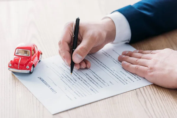 Visão parcial do revendedor de automóveis escrito em contrato de empréstimo perto do carro em miniatura vermelha na mesa de madeira — Fotografia de Stock