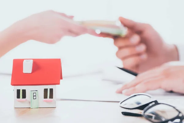 Partial view of businessman taking money from client near house model on tabletop — Stock Photo