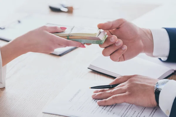 Vista recortada de la mujer dando dinero al gerente de la celebración de la pluma cerca del acuerdo de préstamo - foto de stock