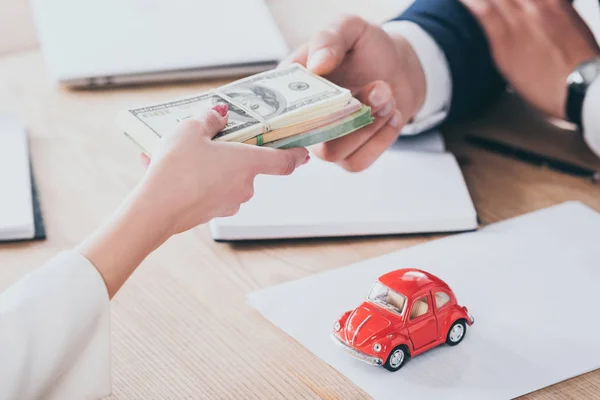 Recortado tiro de cliente dando dinero a empresario cerca de coche de juguete rojo en la mesa - foto de stock
