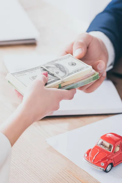 Tiro recortado do gerente que toma notas de dólar do cliente perto do carro de brinquedo vermelho — Fotografia de Stock