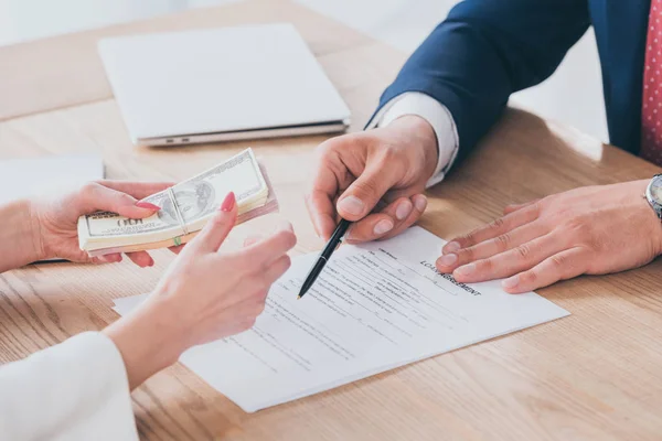 Vista parcial del hombre de negocios señalando el lugar de la firma en el acuerdo de préstamo cerca del cliente que posee dinero - foto de stock