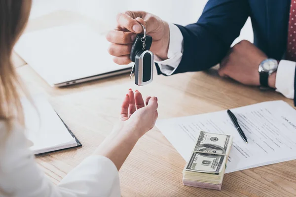Visão parcial do empresário dando chaves de carro ao cliente perto de notas de dólar e contrato de empréstimo — Fotografia de Stock