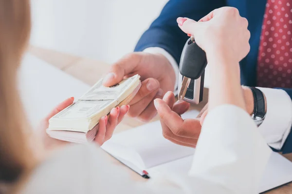 Vue partielle de la femme tenant des clés de voiture tout en donnant de l'argent au concessionnaire automobile — Photo de stock