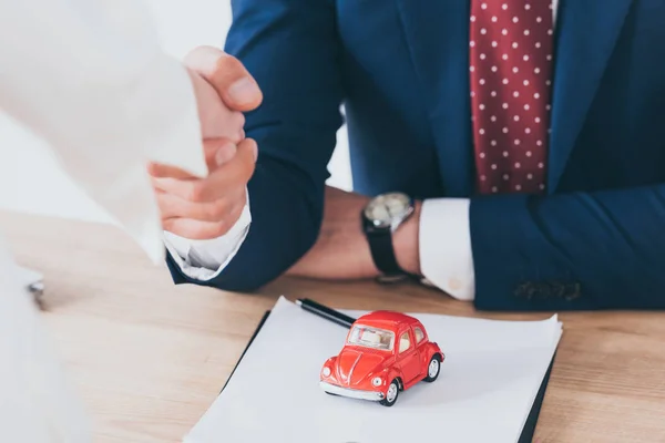 Plan recadré de femme serrant la main avec un homme d'affaires près de jouet voiture rouge — Photo de stock