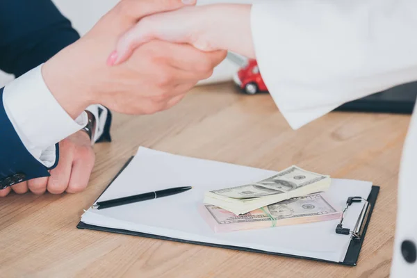 Частковий погляд бізнесмена і клієнта тремтять руки біля доларових банкнот — стокове фото