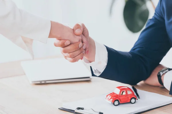 Vue partielle de l'homme d'affaires et du client serrant la main près de la voiture jouet rouge sur la table — Photo de stock