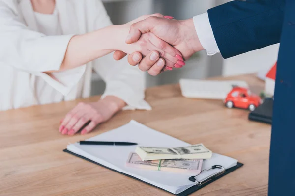 Vue partielle de la femme serrant la main d'un homme d'affaires près des billets en dollars sur la table — Photo de stock
