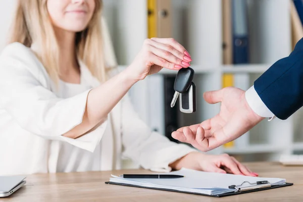 Cropped shot of smiling woman taking car keys from businessman in office — Stock Photo