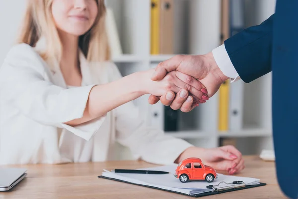 Partial view of smiling woman shaking hands with car dealer in office — Stock Photo