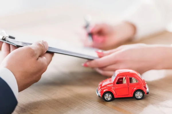 Cropped shot of car dealer giving clipboard to client near miniature car — Stock Photo