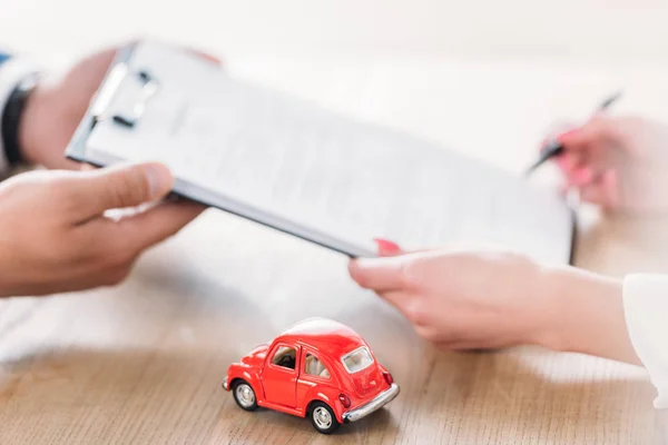 Teilansicht von Autohändler gibt Clipboard an Kunden in der Nähe von Miniatur-Auto — Stockfoto