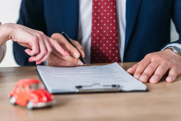 Partial view of car deal pointing at signature place in loan agreement near client holding pen — Stock Photo