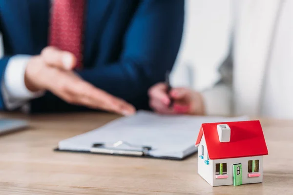 Vue partielle de l'homme d'affaires montrant la place de signature dans l'accord de prêt au client tenant stylo près du modèle de maison — Photo de stock