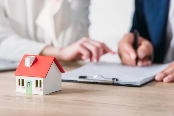 Cropped shot of businesswoman and client signing loan agreement near house model on table — Stock Photo