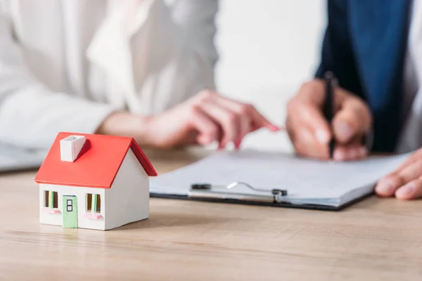 Tiro cortado de empresária e cliente assinar contrato de empréstimo perto do modelo de casa na mesa — Fotografia de Stock