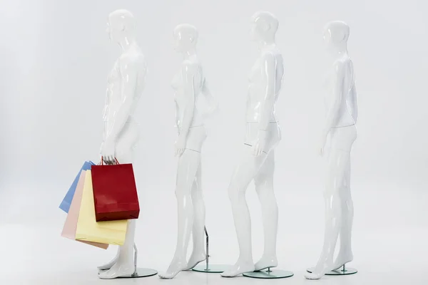 Row of white mannequins with shopping bags on grey — Stock Photo