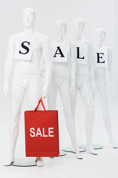 White mannequins with sale lettering on papers and shopping bag on grey — Stock Photo