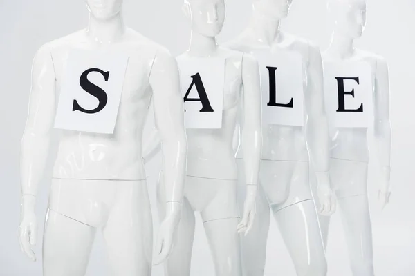 Papers with sale lettering on white plastic mannequins isolated on grey — Stock Photo