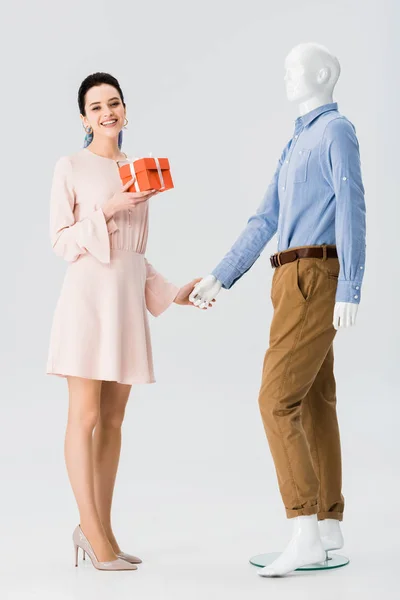 Beautiful girl with gift box holding hands with mannequin isolated on grey — Stock Photo