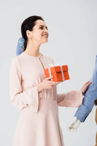 Hermosa chica con caja de regalo sonriendo cerca maniquí aislado en gris - foto de stock