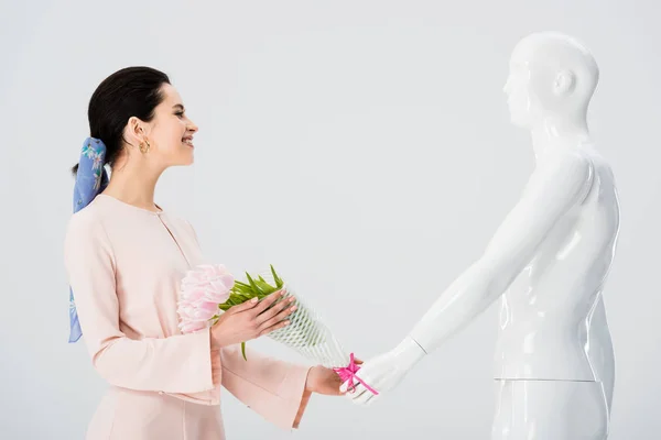 Beautiful girl taking flower bouquet from mannequin isolated on grey — Stock Photo