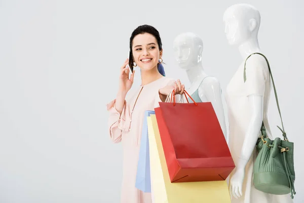 Junge Frau mit Einkaufstaschen spricht auf Smartphone neben Schaufensterpuppen isoliert auf grau — Stockfoto
